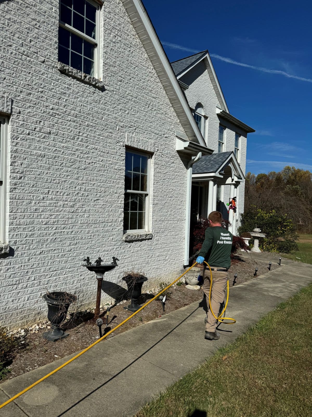 A Planet Friendly Pest Control technician applying a targeted exterior barrier treatment along a Southern Maryland home's foundation
