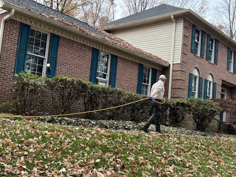 A Planet Friendly Pest Control technician applying a targeted exterior treatment along a brick home's foundation