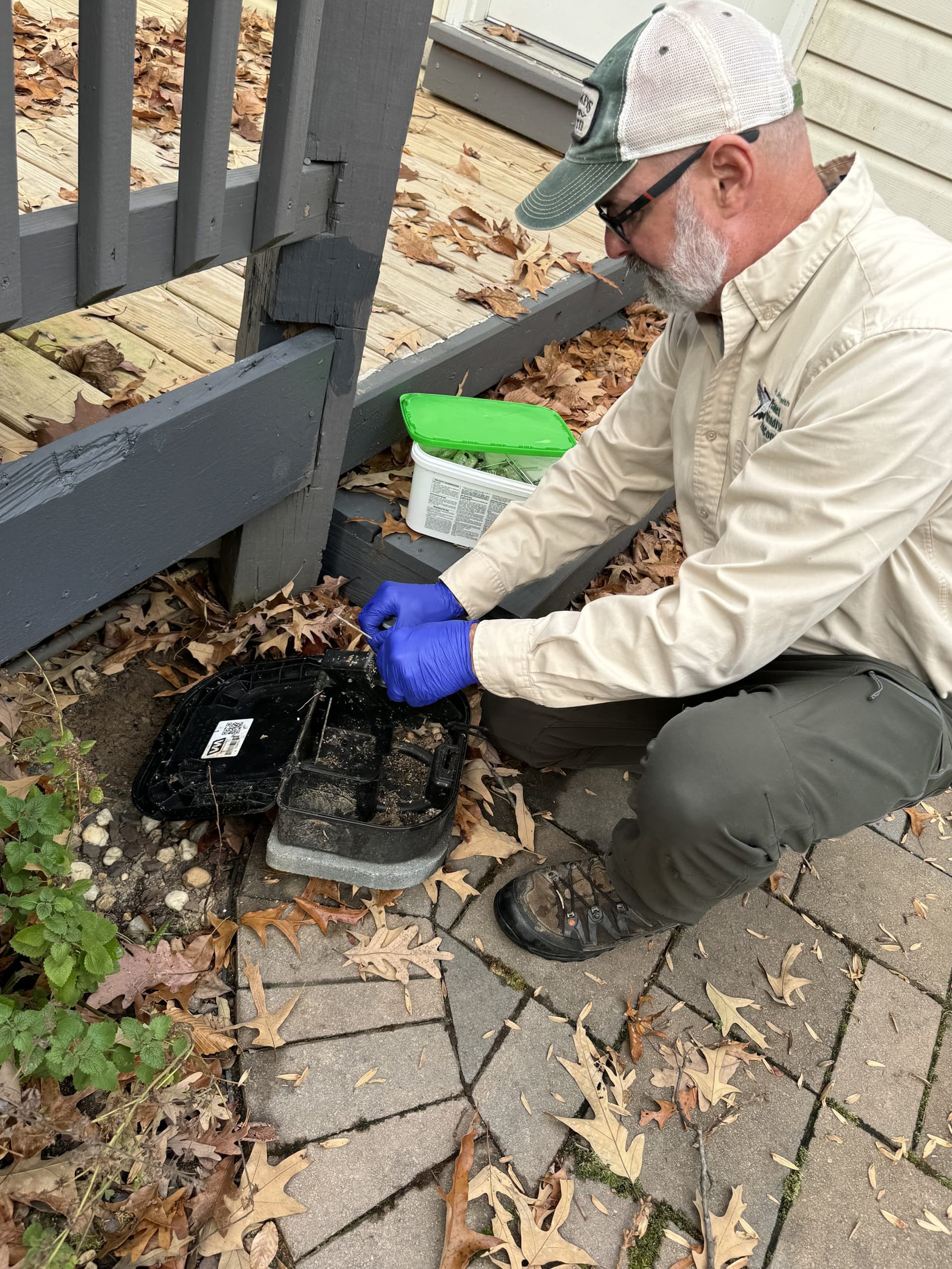 A Planet Friendly technician servicing a rodent bait station near a deck